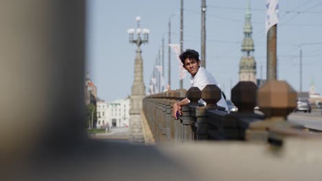 Stylish-Indian-traveler-enjoys-beauty-of-Riga-downtown-and-bridge,-side-view