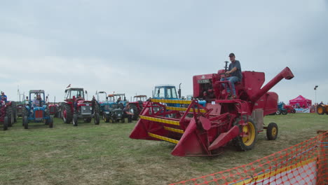 Red-Massey-Ferguson-Combine-Driving-At-The-Field-During-Exhibition-With-Classic-Farm-Tractors-Lined-up-In-Background