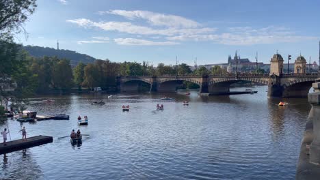 Handheld-shot-of-Paddleboats-on-River-Vltava-in-Prague-on-a-sunny-saturday-afternoon-with-the-Legion-Bridge-in-the-background,-September-2022
