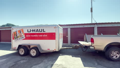 Ford-pickup-truck-pulls-U-Haul-trailer-by-red-storage-units