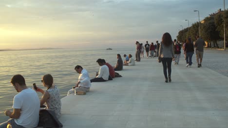 Establisher-shot-of-people-sitting-enjoying-astonishing-sunset-in-Zadar,-Croatia