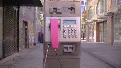 Dolly-shot-of-an-old-street-pay-phone-in-pink-color-with-rusty-spots-in-the-shopping-street-in-cologne-germany-on-a-beautiful-sunny-day