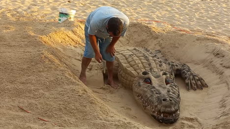 Man-makes-a-sculpture-of-a-sand-crocodile-on-the-beach,-very-beautiful