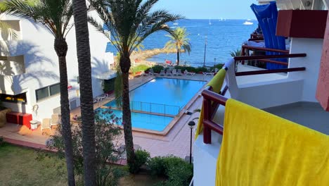 Summer-holiday-rental-vacation-apartments-with-balconies-in-Ibiza-Spain,-nice-swimming-pool-with-palm-trees-and-sea-view,-4K-shot