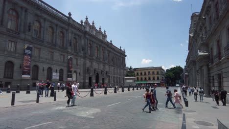 Eine-Der-Straßen-In-Der-Innenstadt-Von-Mexiko-Stadt-Mit-Vorbeifahrenden-Fahrzeugen-Und-Touristen,-Die-Vorbeigehen,-Und-Dem-Nationalmuseum-Für-Kunst-Im-Hintergrund