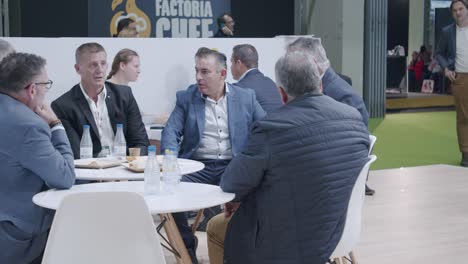 Group-of-professional-men,-sitting-at-table,-casual-discussion,-at-food-trade-show
