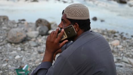 Pakistanischer-Muslimischer-Mann-Saß-Neben-Dem-Fluss-Und-Telefonierte-In-Sindh-Mit-Dem-Handy