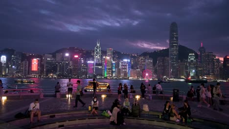 Scharen-Von-Einheimischen-Und-Touristen-Sind-An-Der-Uferpromenade-Von-Victoria-Harbour-Zu-Sehen,-Während-Sie-Die-Nächtliche-Aussicht-Auf-Die-Skyline-Der-Wolkenkratzer-Der-Insel-Hongkong-Genießen