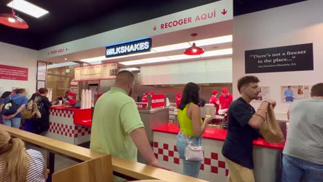 Five-Guys-fast-food-burger-restaurant,-people-waiting-for-their-order,-employees-working-and-cooking,-4K-shot