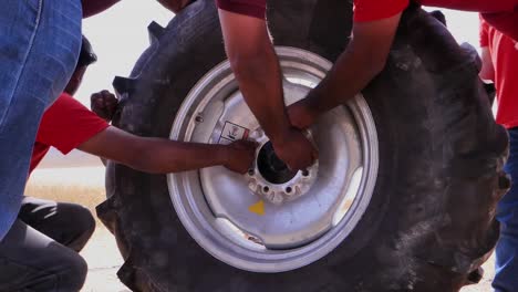 Low-Angle-View-Of-People-Manually-Screwing-Bolts-Into-Large-Tyre-Of-Center-Pivot-Irrigation-System