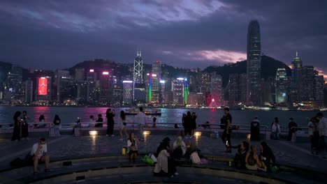 Menschen-Sind-An-Der-Uferpromenade-Von-Victoria-Harbour-Zu-Sehen,-Während-Sie-Den-Nächtlichen-Blick-Auf-Die-Skyline-Der-Wolkenkratzer-Von-Hong-Kong-Genießen