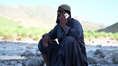 Pakistanischer-Muslimischer-Mann-Saß-Neben-Dem-Fluss-Und-Telefonierte-Mit-Einer-Zigarette-In-Der-Hand-In-Sindh