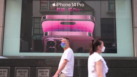 Chinese-pedestrians-walk-past-a-commercial-advertisement-from-the-American-multinational-technology-company,-Apple,-showcasing-the-iPhone-14-Pro-smartphone-in-Hong-Kong