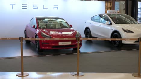 Chinese-shoppers-walk-past-the-American-electric-automaker-company,-Tesla-Motors,-showroom-displaying-electric-vehicles-such-as-model-X-and-Y-cars-at-a-retail-shopping-mall-in-Hong-Kong