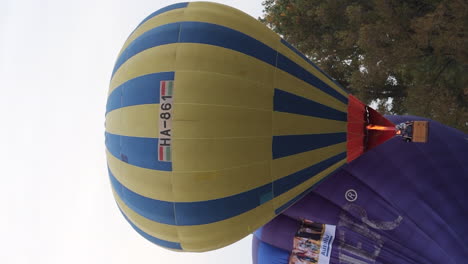 Vertical-video-of-yellow-hot-air-balloon-lifting-off,-rising-above-trees