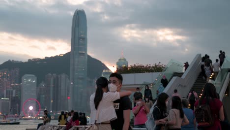Ein-Paar-Umarmt-Sich-Und-Zeigt-Ihren-Zug,-Während-Sie-Den-Abend,-Den-Sonnenuntergang-Und-Die-Skyline-Der-Wolkenkratzer-Der-Insel-Hong-Kong-Genießen