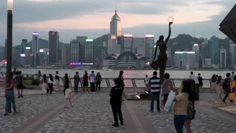 People-are-seen-at-the-Victoria-Harbour-waterfront-as-they-enjoy-their-evening,-sunset,-and-skyline-view-of-Hong-Kong-Island-skyscrapers