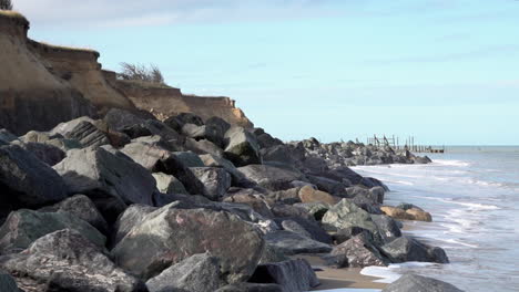 Waves-roll-in-from-the-North-Sea-on-to-a-beach-protected-by-a-sea-defence-of-granite-rocks-on-the-Norfolk-coastline-damaged-by-coastal-erosion
