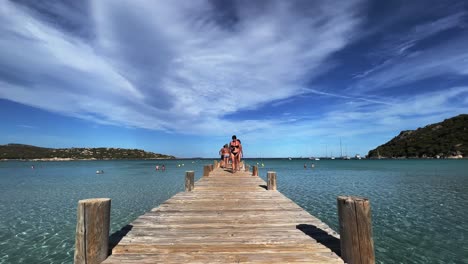 People-enjoy-summer-holiday-at-Santa-Giulia-beach-wooden-pier-in-Corsica-island,-France