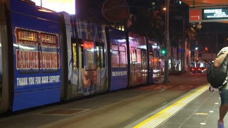 Tram-departing-the-platform-at-cavill-avenue-at-night,-surfers-paradise,-downtown-neighborhood,-Gold-Coast,-Queensland,-Australia