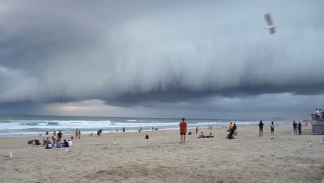 Panning-shot-across-coastal-beach-at-surfers-paradise,-thick-layer-of-ominous-dark-storm-clouds-sweeping-across-the-sky-with-strong-and-raging-wind,-Gold-Coast,-Queensland,-Australia