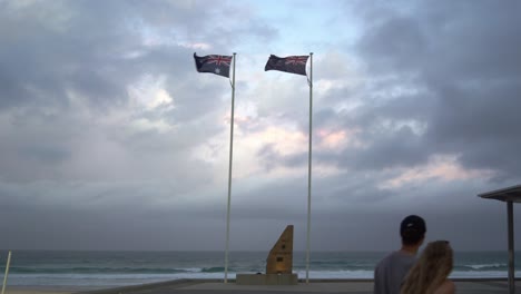 Static-shot-at-ANZAC-memorial-with-Australia-and-New-Zealand-flags-blowing-vigorously-by-the-strong-and-raging-wind-with-dramatic-dark-ominous-clouds-sweeping-across-the-sky-at-Gold-Coast,-Queensland