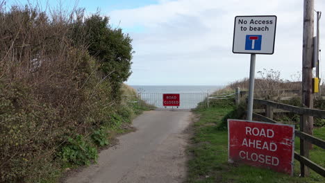 Red-road-closed-signs-and-a-barrier-warn-of-where-coastal-erosion-has-destroyed-a-road-on-the-Norfolk-coastline