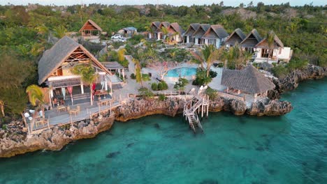 Tourists-at-beach-bungalow-resort-in-swimming-pool-near-the-Indian-Ocean,-Aerial-pedestal-rising-shot