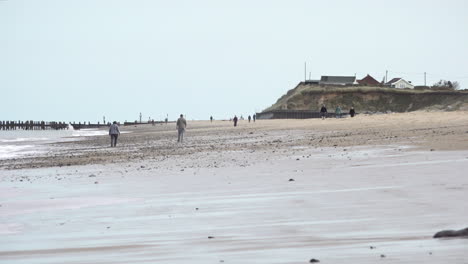 People-walk-along-the-beach-on-the-Norfolk-coastline-damaged-by-coastal-erosion-as-waves-roll-in-from-the-North-Sea