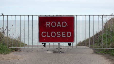 A-red-road-closed-sign-and-barrier-warns-of-where-coastal-erosion-has-destroyed-a-road-on-the-Norfolk-coastline