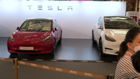 A-family-stands-in-front-of-the-American-automaker-company,-Tesla-Motors,-showroom-displaying-electric-vehicles-such-as-model-X-and-Y-cars-at-a-retail-shopping-mall-in-Hong-Kong