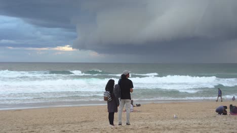 Static-shot-of-coastal-beach-at-surfers-paradise,-thick-layer-of-ominous-dark-storm-clouds-sweeping-across-the-sky,-raging-and-vigorous-waves-crashing-and-hitting-the-shore-at-Gold-Coast,-Queensland