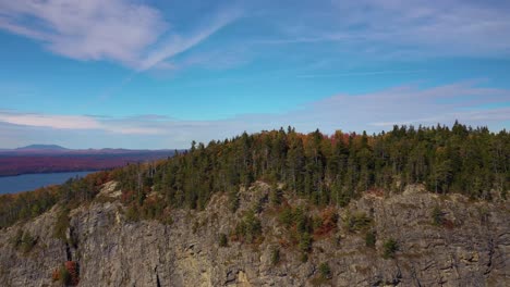 Aerial-slide-to-left-along-top-of-cliff-on-Kineo-Mountain-in-peak-fall-foliage