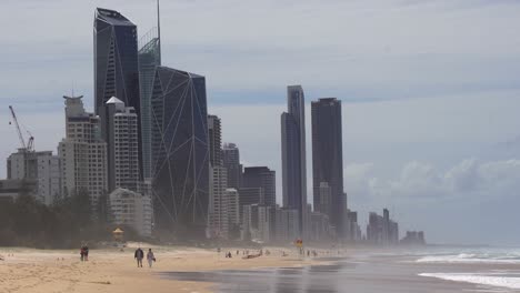 People-strolling-on-the-golden-sandy-beach-with-high-rise-investment-properties-in-the-background,-popular-tourist-destination-in-summer-at-Broadbeach-Gold-coast,-Queensland,-Australia