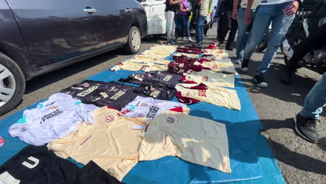 High-angle-shot-over-roadside-vendor-selling-football-jersey-t-shirts-on-sale-before-a-match-in-Universitario,-Monumental,-Ate,-Lima,-Peru-at-daytime
