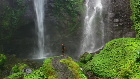 Zoom-Aéreo-Fuera-Del-Hombre-Feliz-Con-Los-Brazos-Extendidos-En-La-Cascada-Sekumpul-En-Bali-Indonesia