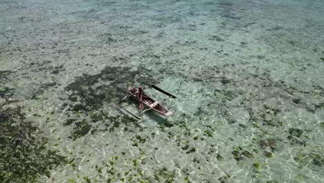 Male-Islander-paddling-canoe-over-the-coral-filled-shallow-lagoon,-Aerial-rising-shot