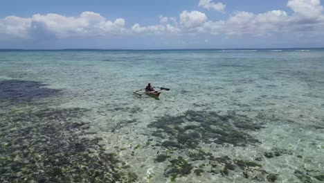 Islander-paddling-canoe-over-the-coral-filled-shallow-lagoon,-Aerial-orbit-around-shot