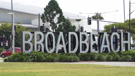 Close-up-shot-of-iconic-Broadbeach-sign,-a-cyclist-cycle-across-Victoria-park-at-daytime,-Queensland,-Australia