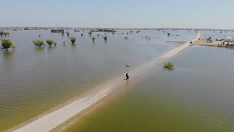 Aerial-View-Of-Flooded-Landscape-In-Maher-With-Drone-Operator-Standing-On-Only-Road-Running-Through-It