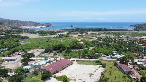 Aerial-rising-over-port-infrastructure-developments,-local-community-houses,-traffic-and-ocean-views-on-the-outskirts-of-capital-Dili-in-rural-Tibar,-Timor-Leste,-Southeast-Asia