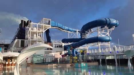 NCL,-Norwegian-Bliss-cruise-ship-pool-deck-and-slides-after-rain-showing-smokestack