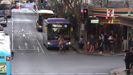 Rappelvoller-Straßenverkehr,-Voller-Busse,-Die-Auf-Der-Adelaide-Street-Fahren,-Fußgänger-Und-Büroangestellte,-Die-An-Der-Kreuzung-Die-Ecke-Der-Edward-Street-Während-Der-Verkehrszeiten-In-Der-Innenstadt-Von-Brisbane-überqueren