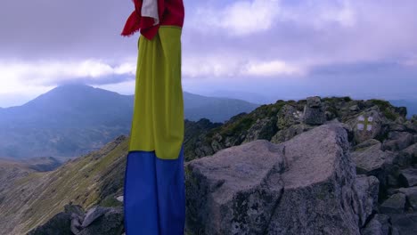 Romanian-flag-at-the-top-of-the-mountain-tied-to-a-pole-with-camera-panning-to-the-right