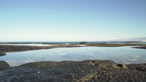Close-up-of-a-tide-pool-and-lava-rock-with-waves-splashing-in-the-distance