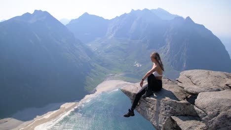 Attractive-woman-with-braided-hair-seated-on-a-rock-ledge-overlooking-the-sea