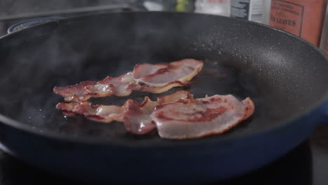 2-bits-of-bacon-cooking-in-frying-pan,-slider-shot