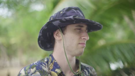 Young-Man-in-park-ranger-explorer-outfit-and-wide-brim-hat-stares-into-the-distance-in-tropical-Jungle