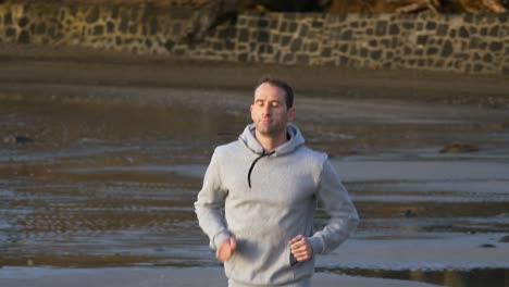 Slow-motion-shot-of-young-caucasian-man-running-on-the-beach-in-Auckland,-New-Zealand