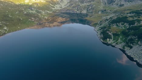 Wide-aerial-drone-above-a-lake-slowly-turning-right-to-a-mountain-range